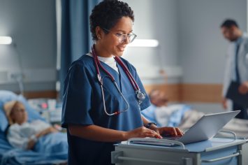 woman-hospital-bed-with-stethoscope-her-neck-looks-laptop